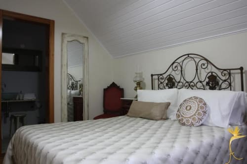 Quarto aconchegante em Casa Estrelícia-Dourada Garcês em São Vicente com cama de ferro ornamentada e roupa branca.