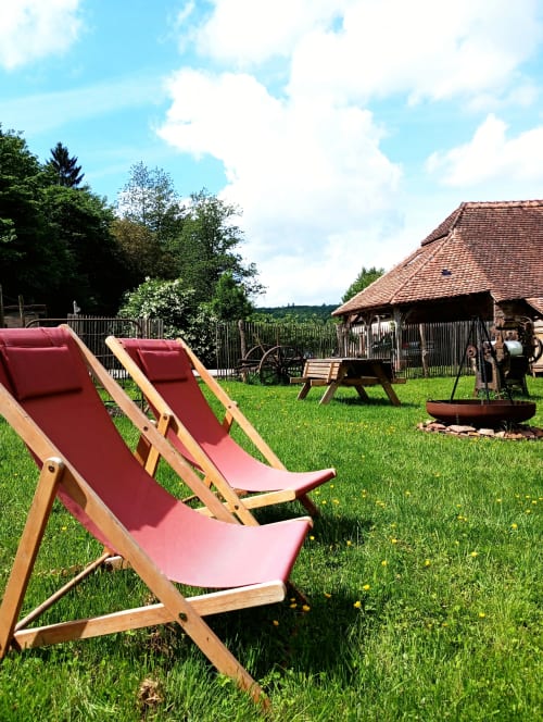 Chaises longues rouges sur la pelouse de la chambre d'hôtes Paulusmühle à Soucht, France, avec vue sur la grange traditionnelle et la campagne