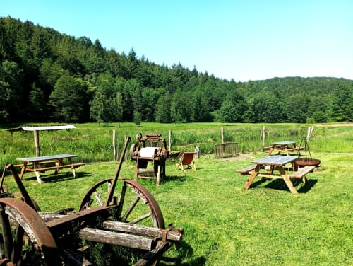 Équipements agricoles rustiques et tables de pique-nique dans une prairie verdoyante à la maison d'hôtes Paulusmühle, Soucht