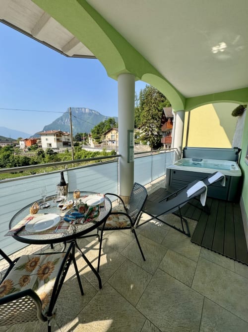 Terrazza di lusso a Ranzo con vista montagna, tavolo da pranzo, vasca idromassaggio e lettini sotto pergolato verde