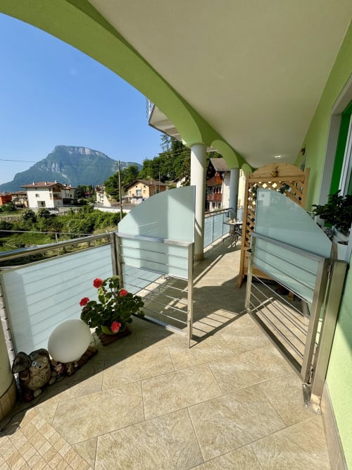 Terrazza soleggiata di Villa Zoe con vista sulle montagne, fiori rossi e pergolato verde a Ranzo, Italia