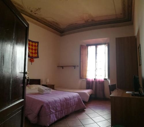 Camera tripla di Casa di Alfredo B&B a Siena con due letti, armadio in legno e finestra con tende viola
