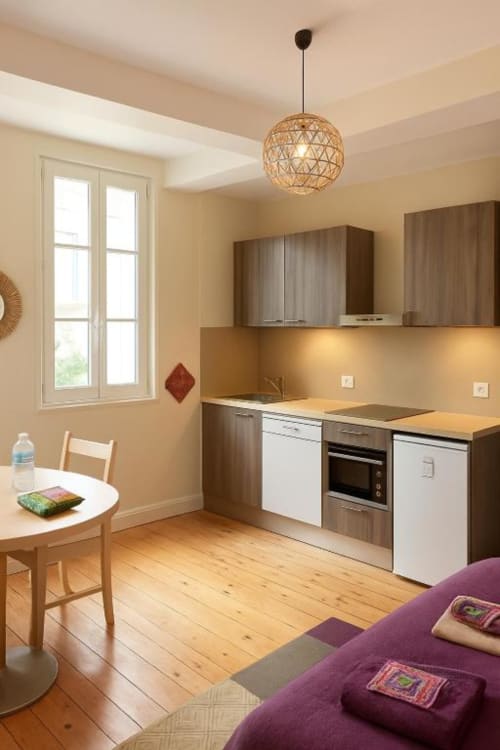 Cuisine de studio moderne avec parquet, murs beige, mobilier blanc et marron, suspension, table à manger