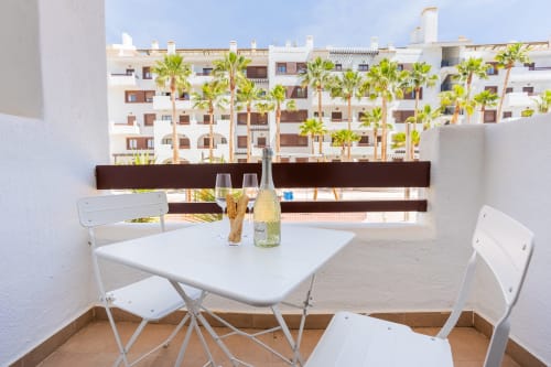 Comedor en terraza de Haus Holiday Homes con mesa blanca, sillas, botella de vino, vista a la piscina y palmeras en San Pedro