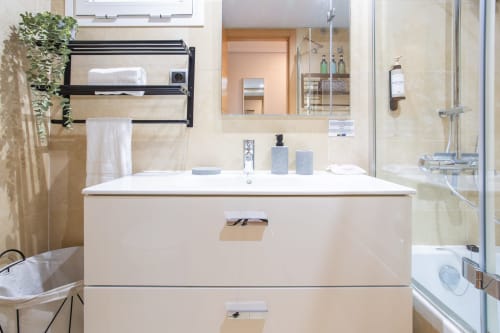 Baño moderno con tocador blanco, toallero negro, espejo y ducha abierta en apartamento Haus Holiday Homes, San Pedro