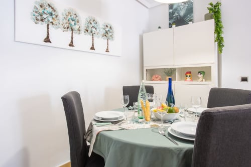 Elegante comedor con mesa redonda, sillas grises, muebles blancos y cuatro obras de arte con árboles en Haus Holiday Homes, San Pedro