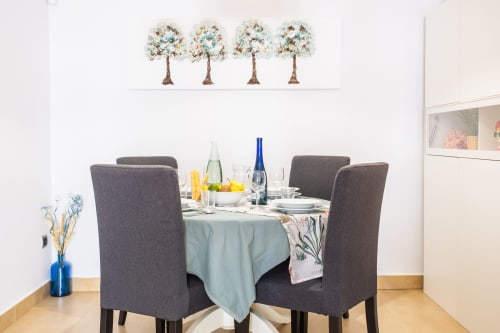 Elegante comedor en apartamento Haus Holiday Homes de San Pedro del Pinatar con sillas grises, mesa servida y arte mural.