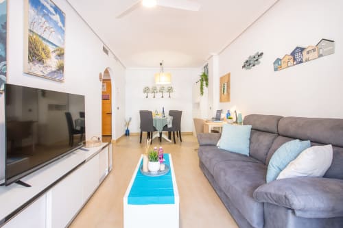 Moderno salón en apartamento de San Pedro del Pinatar con sofá gris, TV plana, comedor y decoración costera