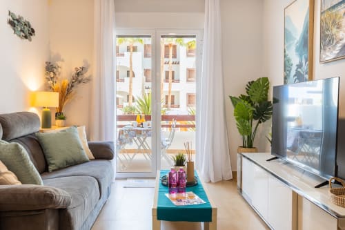 Elegante sala de estar en apartamento de San Pedro del Pinatar con sofá gris, TV, planta y balcón con vista a piscina