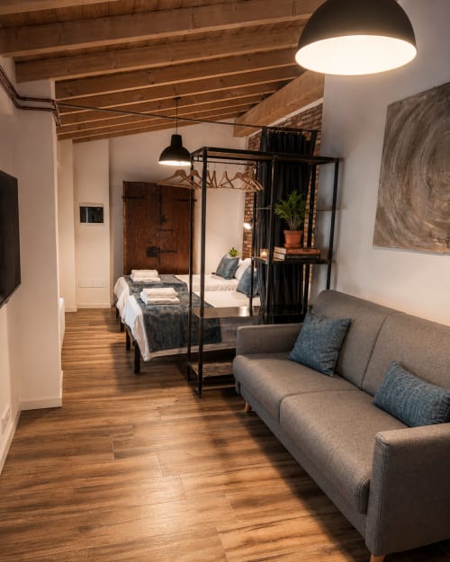 Modernes Loft in Bergamos Stadtzentrum mit Holzbalken, grauem Sofa, schwarzem Himmelbett und Pendelleuchten