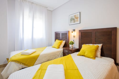Dos camas individuales con detalles amarillos en el luminoso dormitorio del apartamento de Haus Holiday Homes, San Pedro del Pinatar