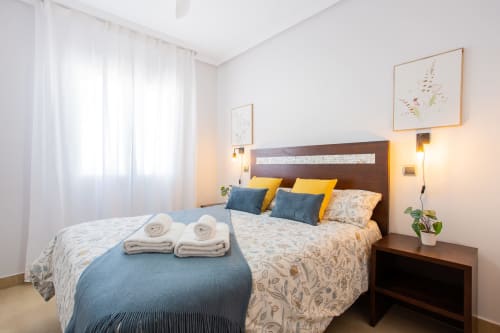 Moderno dormitorio en Haus Holiday Homes, San Pedro del Pinatar, con cama doble, almohadas amarillas, mantas azules y vista al jardín