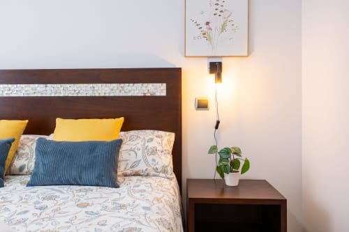 Dormitorio moderno con cama de marco de madera oscura, almohadas amarillas, ropa de cama estampada, cojín azul rayado, mesilla de noche de madera con