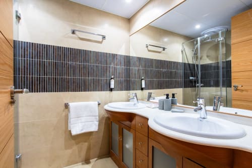 Baño moderno con doble lavabo, pared de azulejos negros, muebles de madera y ducha de cristal en Haus Holiday