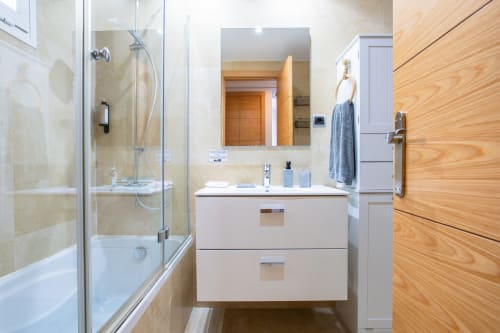 Baño moderno con ducha, tocador blanco, espejo y paneles de madera en apartamento Haus Holiday Homes, San Pedro del