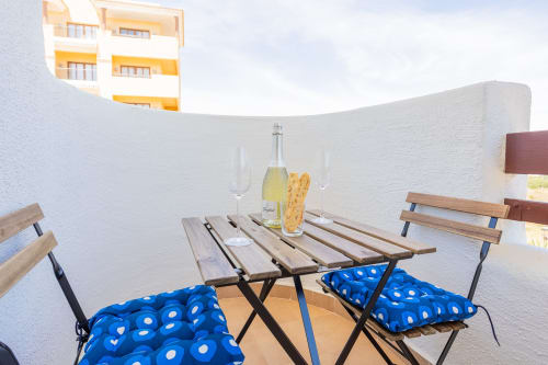 Terraza privada en Haus Holiday Homes con mesa de madera, sillas azules acolchadas, botella de champagne y apartamento amarillo