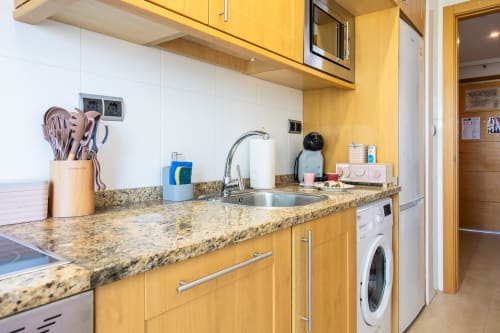 Cocina moderna con muebles dorados, encimera de granito, fregadero y lavadora en apartamento de Haus Holiday Homes, San Pedro
