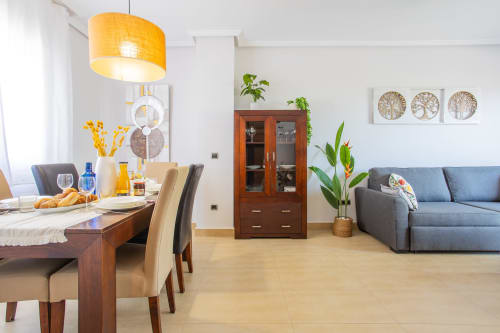 Moderno salón-comedor con muebles de madera, sofá gris, lámpara colgante amarilla y plantas de interior en Haus