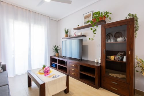 Sala moderna con TV, muebles de madera, plantas en maceta y vitrina de cristal en apartamento Pura Vida II de Haus Holiday