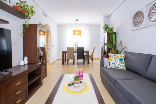 Sala moderna con sofá gris, área de comedor, muebles de madera y plantas en maceta del apartamento Pura Vida II