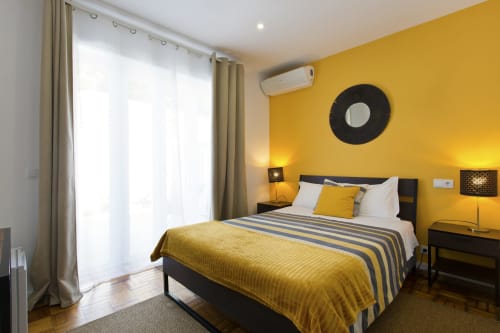 Modern double bedroom at 100 Contos in Porto with yellow accent walls, striped bedding, black furniture, and city view