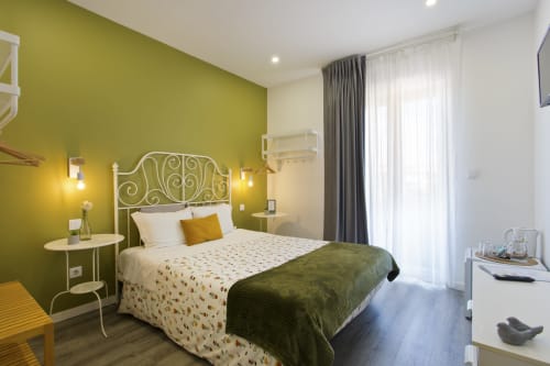 Bright double bedroom with lime green accent wall, ornate iron headboard, and balcony at 100 Contos Porto