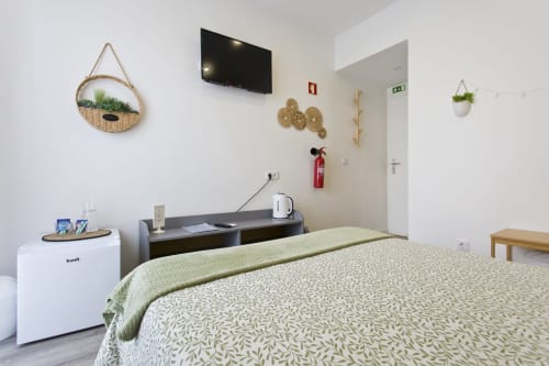 Modern bedroom at 100 Contos B&B Porto with bed, desk, wall-mounted TV, plants, and city view