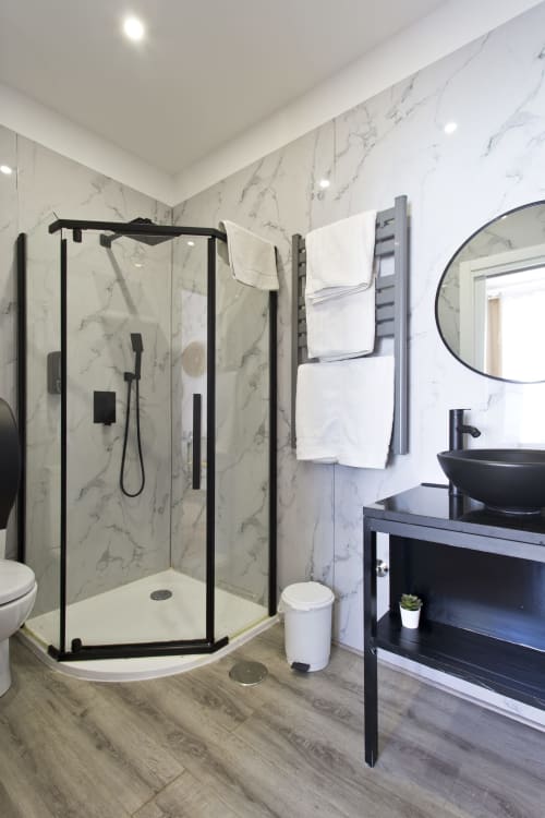 Modern bathroom in 100 Contos Porto B&B with black-framed shower, marble walls, black vessel sink, round mirror, and towel
