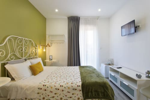 Modern double bedroom with olive accent wall, ornate headboard, and city view balcony at 100 Contos hotel in Porto