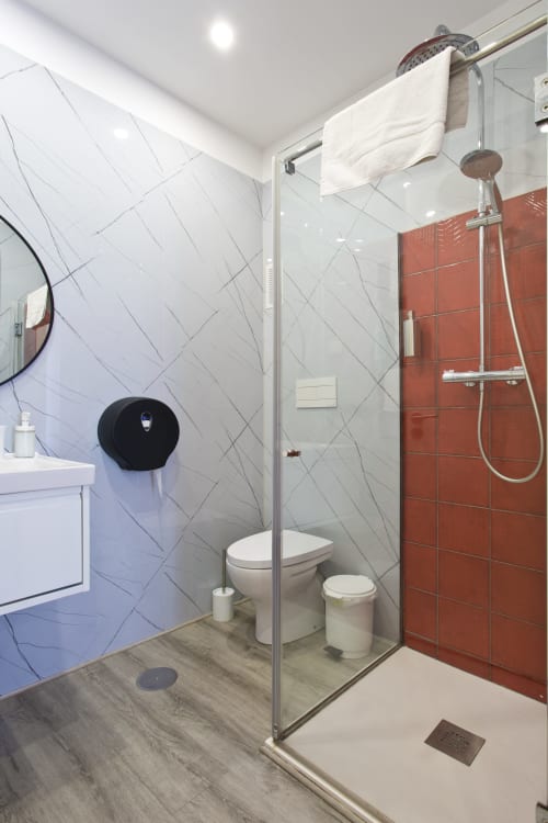 Modern bathroom in 100 Contos Porto BnB with white marble tiles, red accent wall, glass shower, toilet, and white vanity