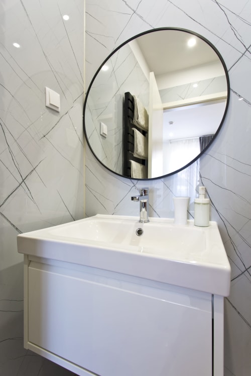Modern bathroom sink with round black-framed mirror at 100 Contos B&B in Porto, Portugal