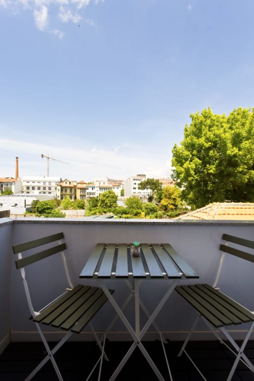 Rooftop terrace at 100 Contos Porto with city views, two chairs, table, and green trees surrounding historic buildings