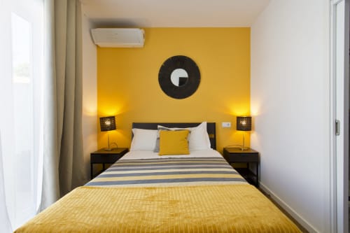 Bright yellow bedroom at 100 Contos B&B in Porto with double bed, black nightstands, warm lighting, and modern amenities