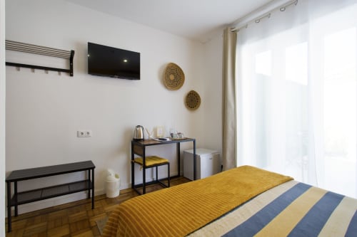 Modern double bedroom at 100 Contos Porto with yellow striped bed, flat-screen TV, desk, and natural light from balcony