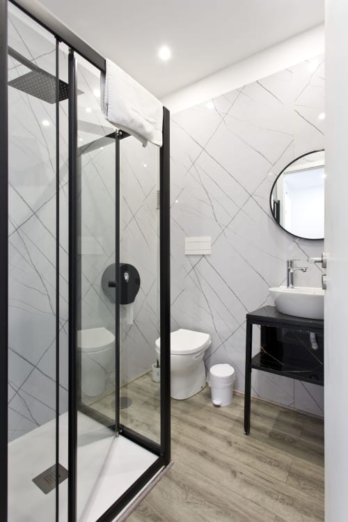 Modern bathroom in 100 Contos Porto bnb with black-framed glass shower enclosure, white sink, toilet, and herringbone tile