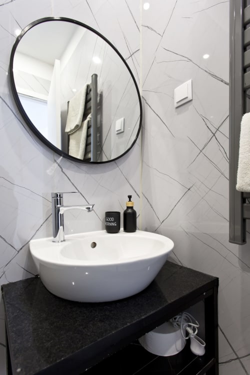 Modern bathroom vanity with white round sink, black countertop, circular mirror, and geometric tile wall at 100 Contos bnb in