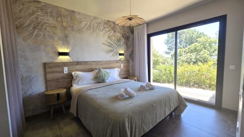Modern villa bedroom in Lecci with bed, botanical wall mural, pendant light, and glass doors overlooking trees