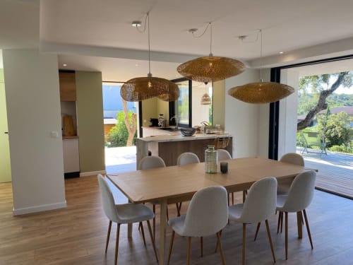 Salle à manger contemporaine avec table en bois, luminaires suspendus tissés, îlot de cuisine et vue sur la terrasse de la villa Casa di Sadrea