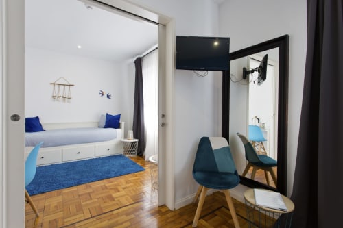 Modern family bedroom at 100 Contos, Porto. Blue accents, wooden floors, TV, storage bed, mirror, and contemporary