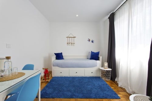 Bright family room at 100 Contos BnB in Porto with white bed, blue accents, wooden floor, and city view windows