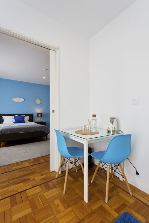 Modern family room at 100 Contos Porto with blue chairs, work desk, wooden flooring, and bedroom view through doorway