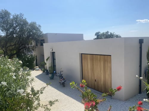 Entrée de villa moderne blanche à Casa di Sadrea à Lecci avec porte en bois, cour de gravier, plantes fleuries et moto