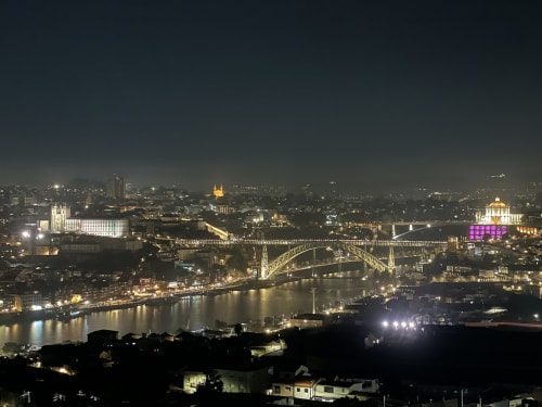 Paisagem noturna do Porto com ponte iluminada, rio e arquitetura histórica vista da Torre dos Clérigos