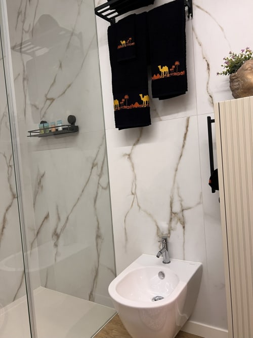 Banheiro moderno no apartamento Douro Tower, Timeless Vacations, com paredes em mármore, pia branca e toalheiro com detalhes pretos
