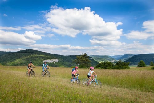 Famille à vélo dans les prairies près du Refuge des Brumes, montagnes des Vosges en arrière-plan