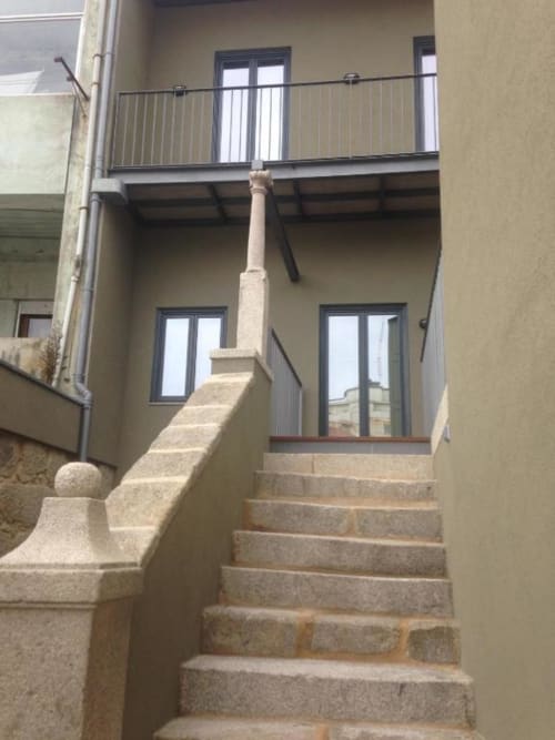 Escadaria de pedra levando à entrada moderna de apartamento com corrimãos metálicos em edifício do Porto