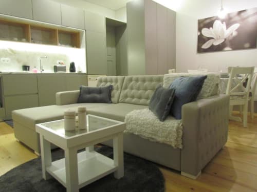 Sala de estar moderna com sofá seccional bege, mesa de centro branca, kitchenette e vista para o jardim no Porto.