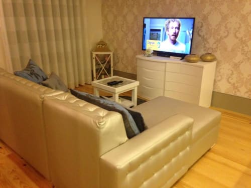 Sala de estar moderna com sofá creme, TV de tela plana, cômoda branca e piso de madeira no apartamento do Porto na Timeless