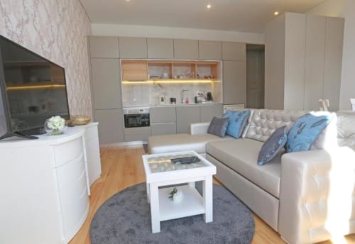 Apartamento moderno em plano aberto no Porto com sofá bege, cozinha branca, área de refeições e pisos em madeira na Timeless Vacations