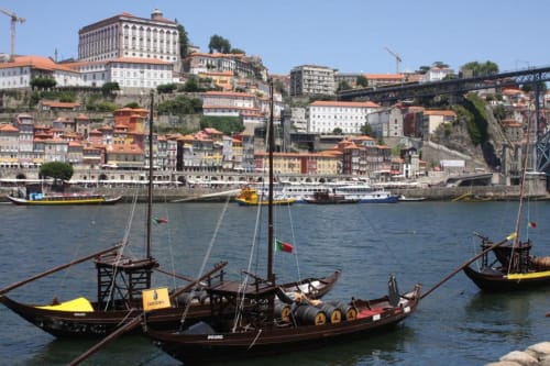 Barcos de madeira tradicionais no Rio Douro com a paisagem colorida do Porto e ponte ao fundo